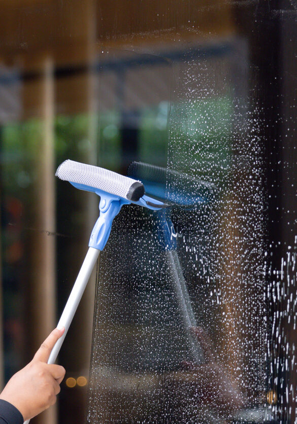 A person is cleaning a window with a squeegee. The window is covered in streaks and the person is using a blue and white squeegee to clean it